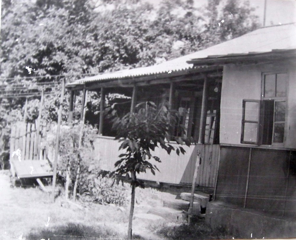 Одноэтажный дом-мазанка с верандой и деревянным забором.